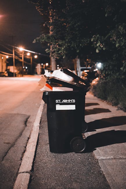 Two large black and white plastic bags filled with waste are placed on the pavement beside a curb, with one bag leaning against the other. The bags appear to contain bulky household or garden rubbish,
